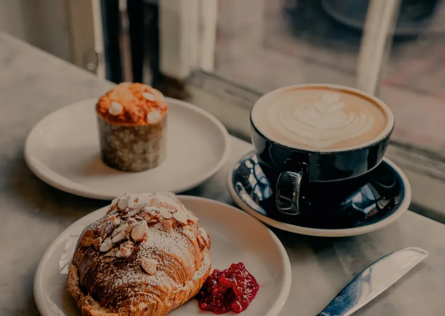 A flat white with latte art beside a muffin and an almond croissant on a café table.
