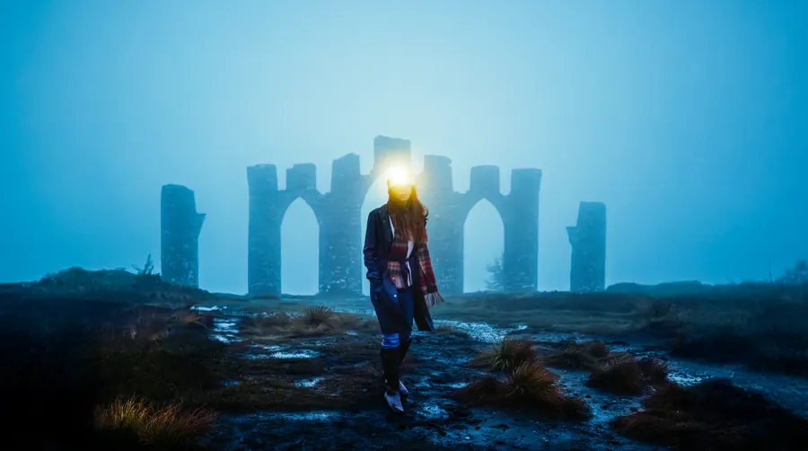 Stone arches in blue mist at night, lit by a single headlamp.