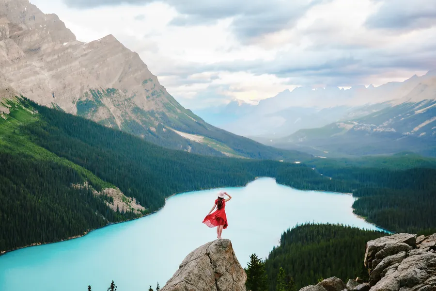 A figure in a red dress on a rock above the turquoise water of Peyto Lake, Banff, with mountains beyond.